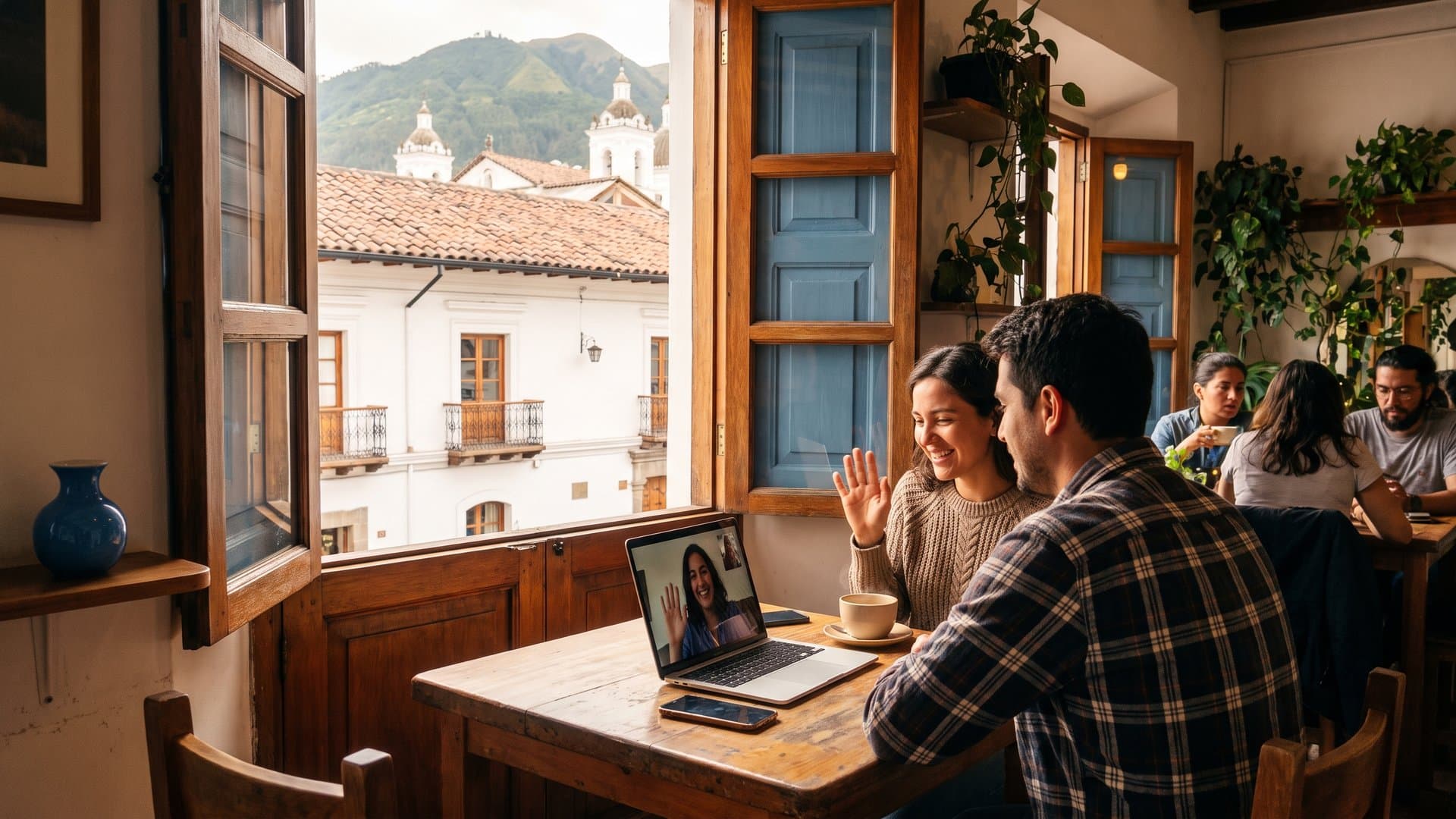Una mesa junto a una ventana abierta con laptop, celular y un café